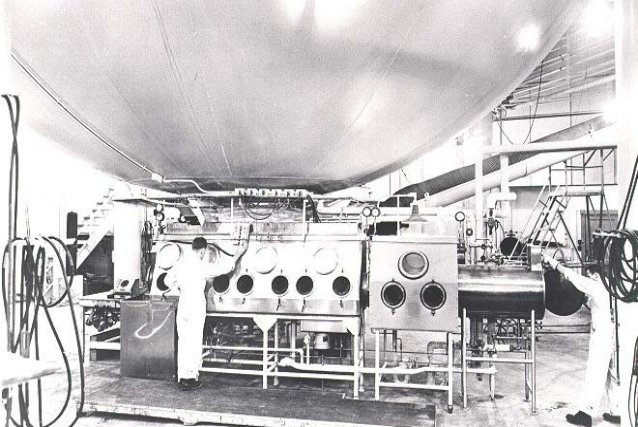 Two men stand in a lab in front of a bench of instruments.