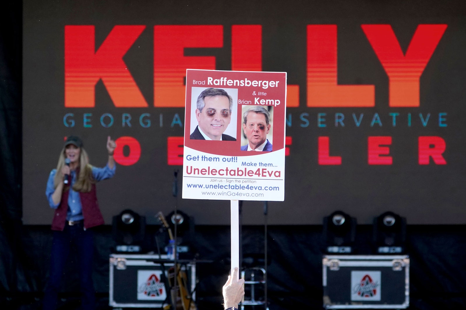 A Loeffler event attendee holds a sign showing Kemp and Raffensperger beat up.