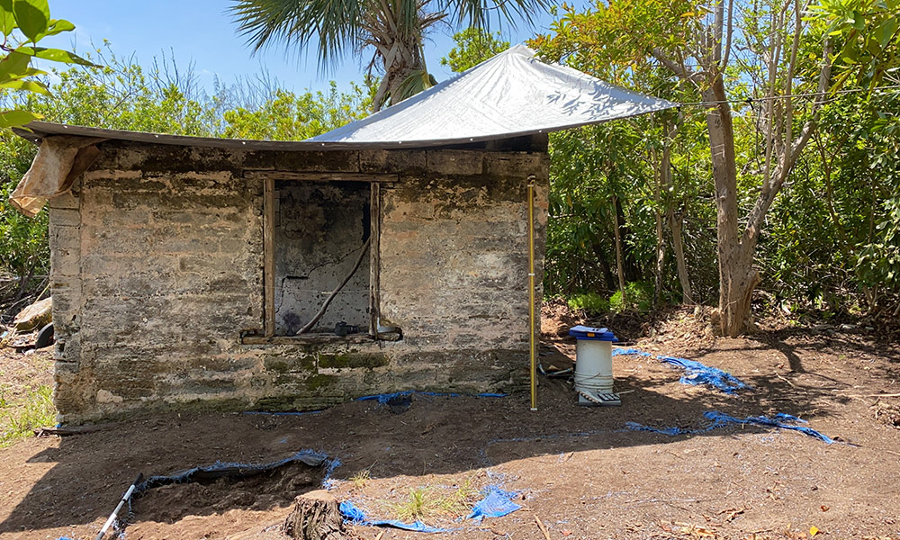 an archaeological digging site on Smith Island, with an old stone building in the forground and palm trees and ocean in the background.