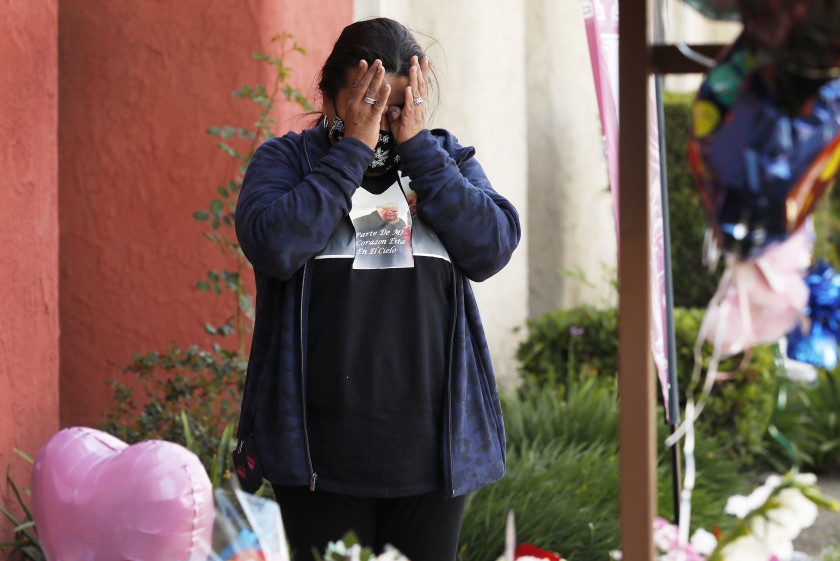 A woman wipes away tears while standing next to a memorial.