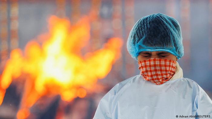 A boy in a protective suit in front of a funeral pyre