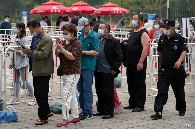 A security guard watches residents wearing face masks to help curb the spread of the coronavirus line up to receive the…