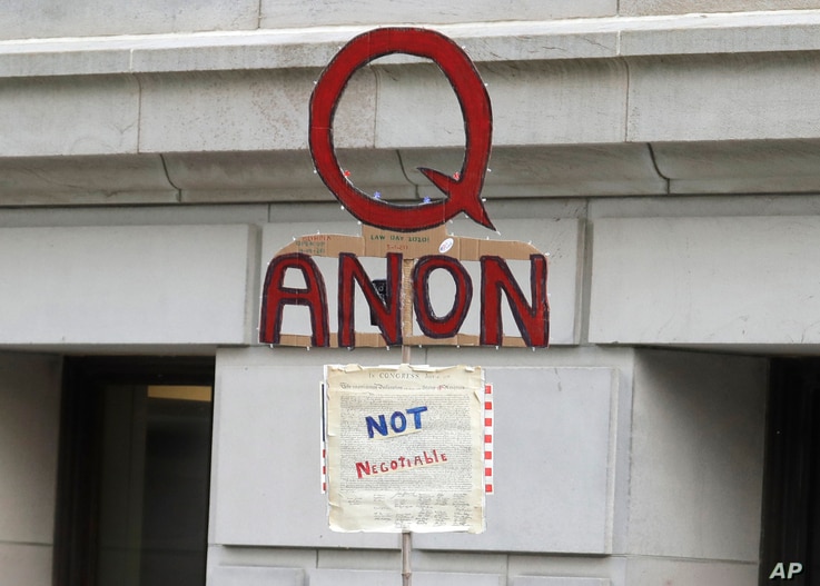 In this May 14, 2020, photo, a person carries a sign supporting QAnon at a protest rally in Olympia, Wash., against Gov. Jay…