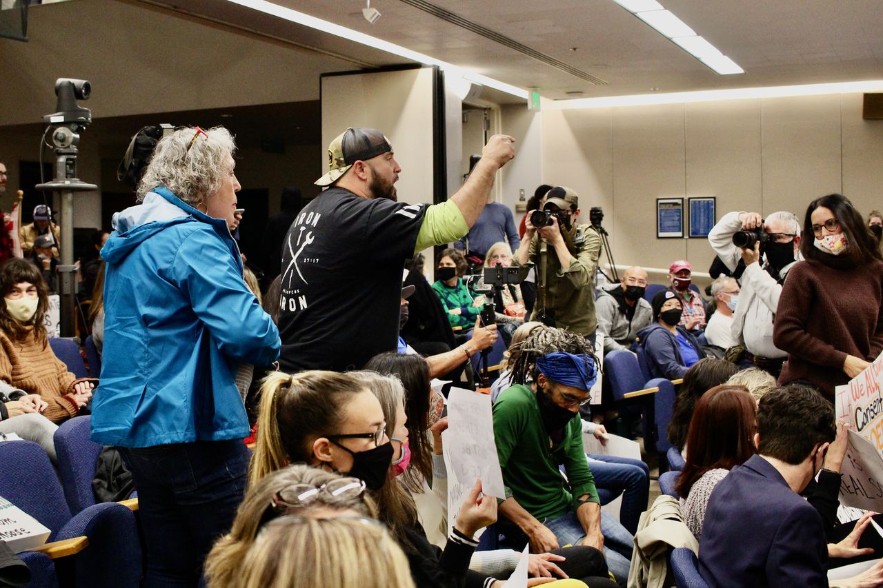 Man stands up in a crowd, pointing a finger and shouting