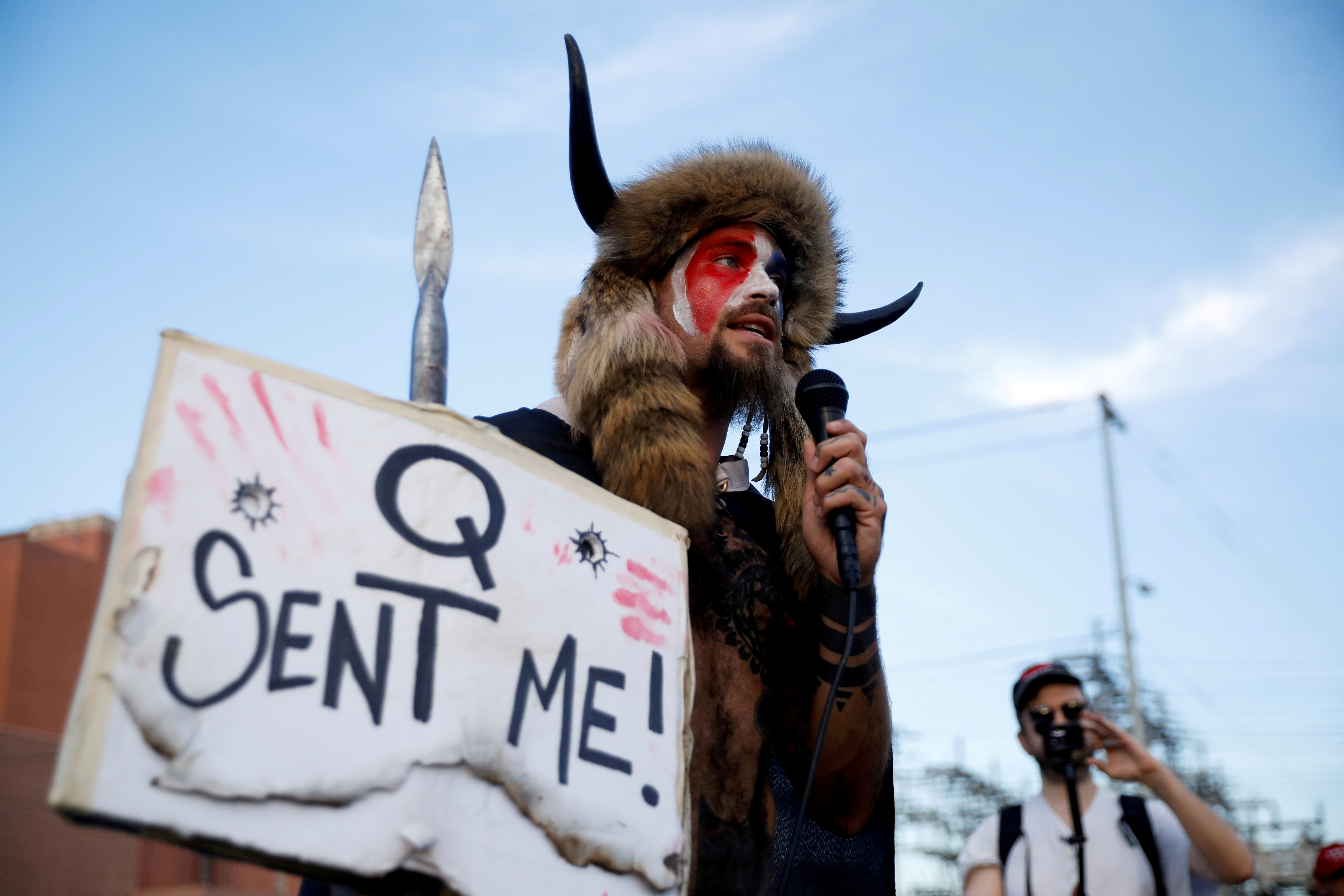 Jacob Chansley, holding a sign referencing QAnon, speaks as supporters of U.S. President Donald Trump gather to protest about the early results of the 2020 presidential election, in front of the Maricopa County Tabulation and Election Center (MCTEC), in Phoenix, Arizona November 5, 2020. REUTERS/Cheney Orr/File Photo