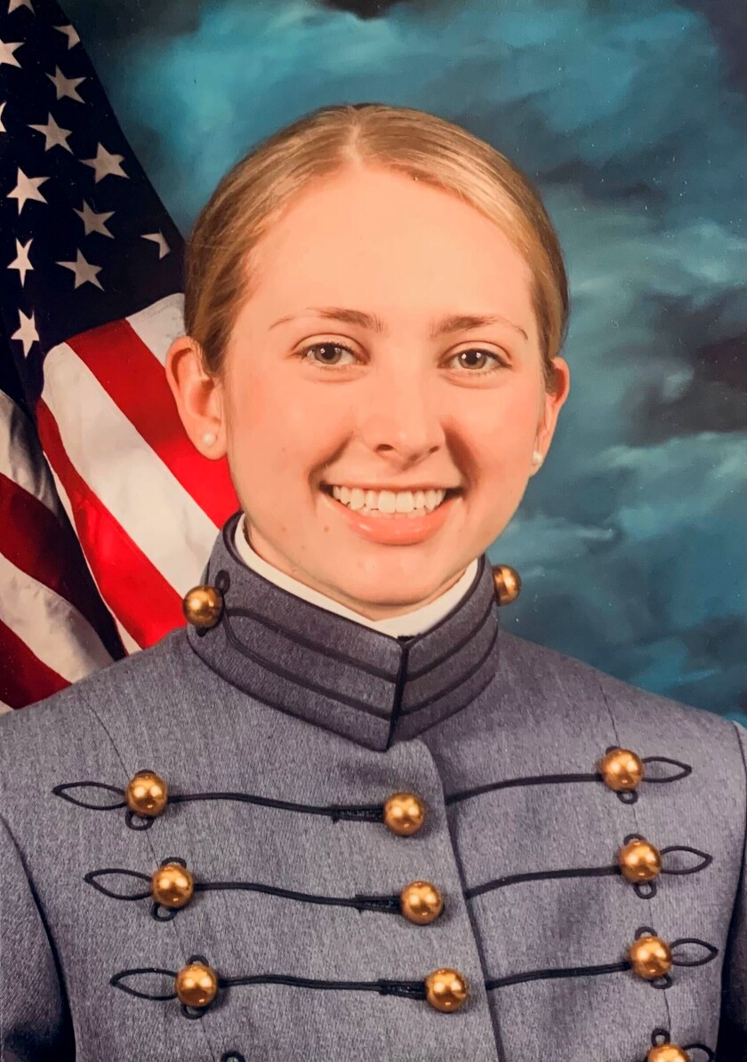 A smiling woman in a gray uniform in front of a U.S. flag