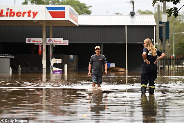 Conspiracy theorists claim the motive for 'elites' carrying out a 'weather attack', which have seen communities around Byron Bay and Lismore underwater is to move people into 'smart cities'. Pictured: Local residents wade through floodwater in Lismore, NSW