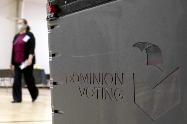 A worker passes a Dominion Voting ballot scanner.