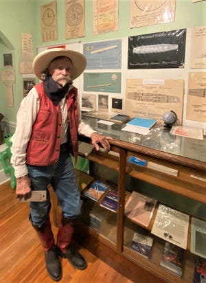 Jim Gray, president of the Geneseo Museum, stands next to a display case in the UFO room at the city museum. On the wall are original drawings by people from around the country who claimed to have had close contact with the spacecraft, which were collected by the museum creator, Dr. Elmer Janzen, and in the case are books authored by believers, including John Dean of Nickerson.