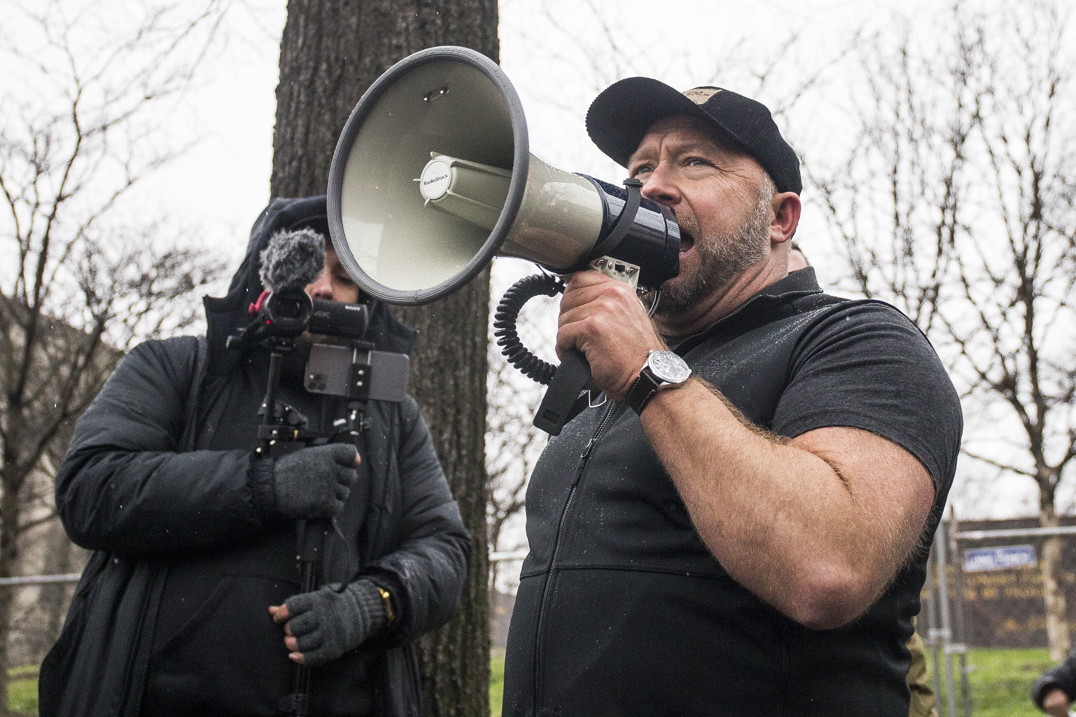 A man dressed in black speaks into a loudspeaker.