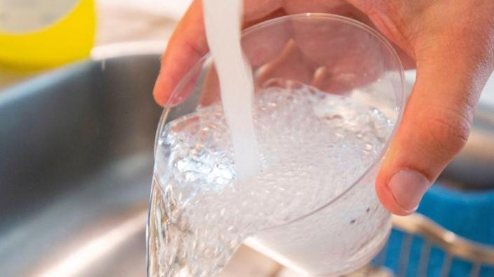 A person holds a cup under tap water and lets the water spill out.