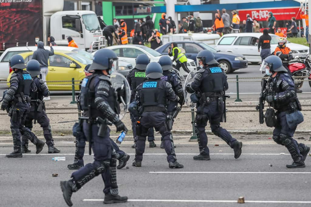 Police in body armour on a road with protesters in the background