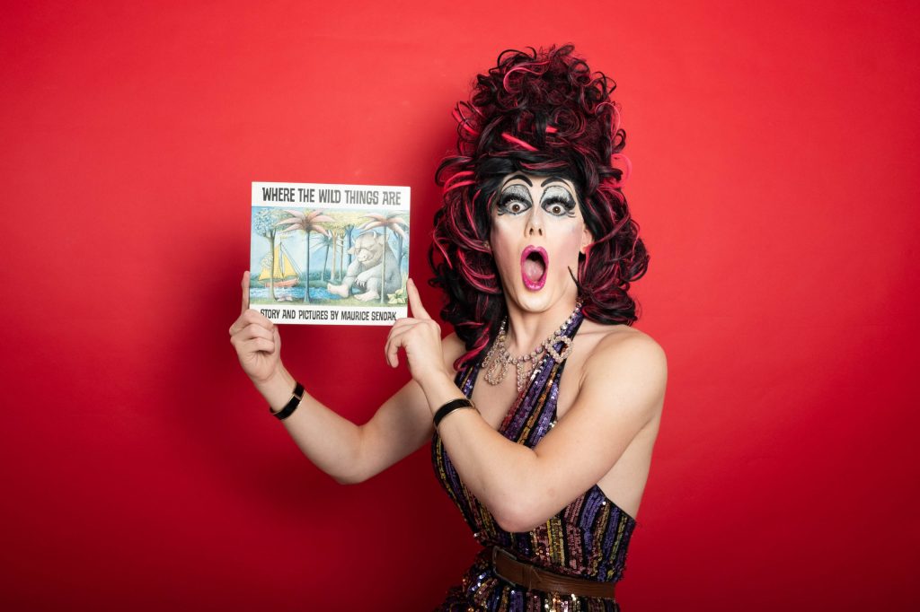 Drag queen Aida H Dee holding up a story book