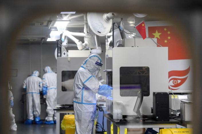 Laboratory technicians wearing personal protective equipment stand at testing stations.