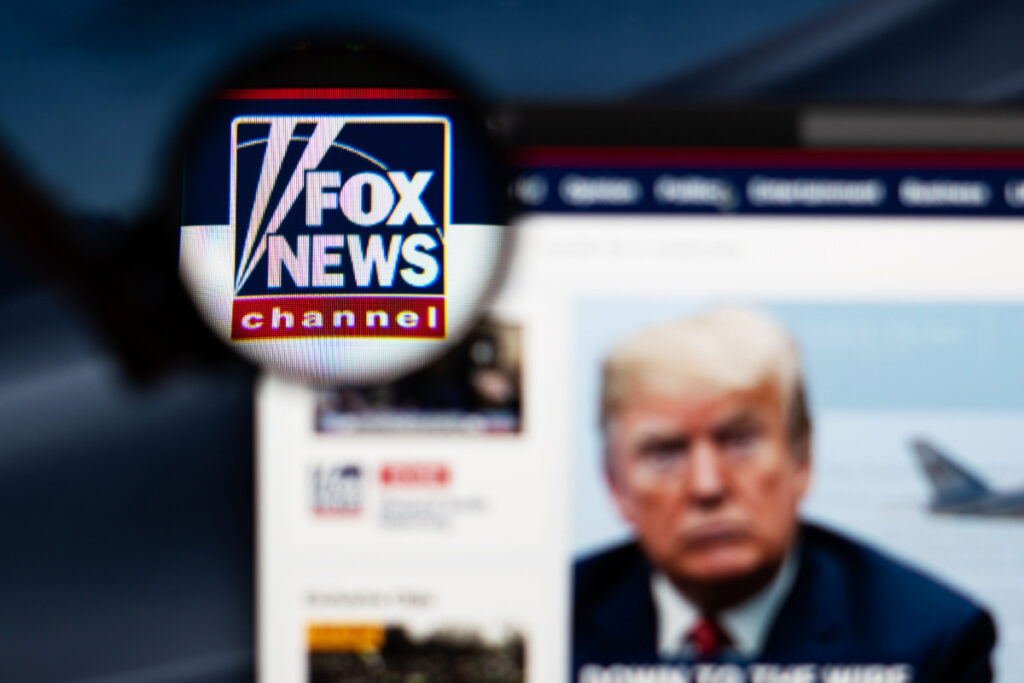 Fox News website homepage. Fox News channel logo visible through a magnifying glass.