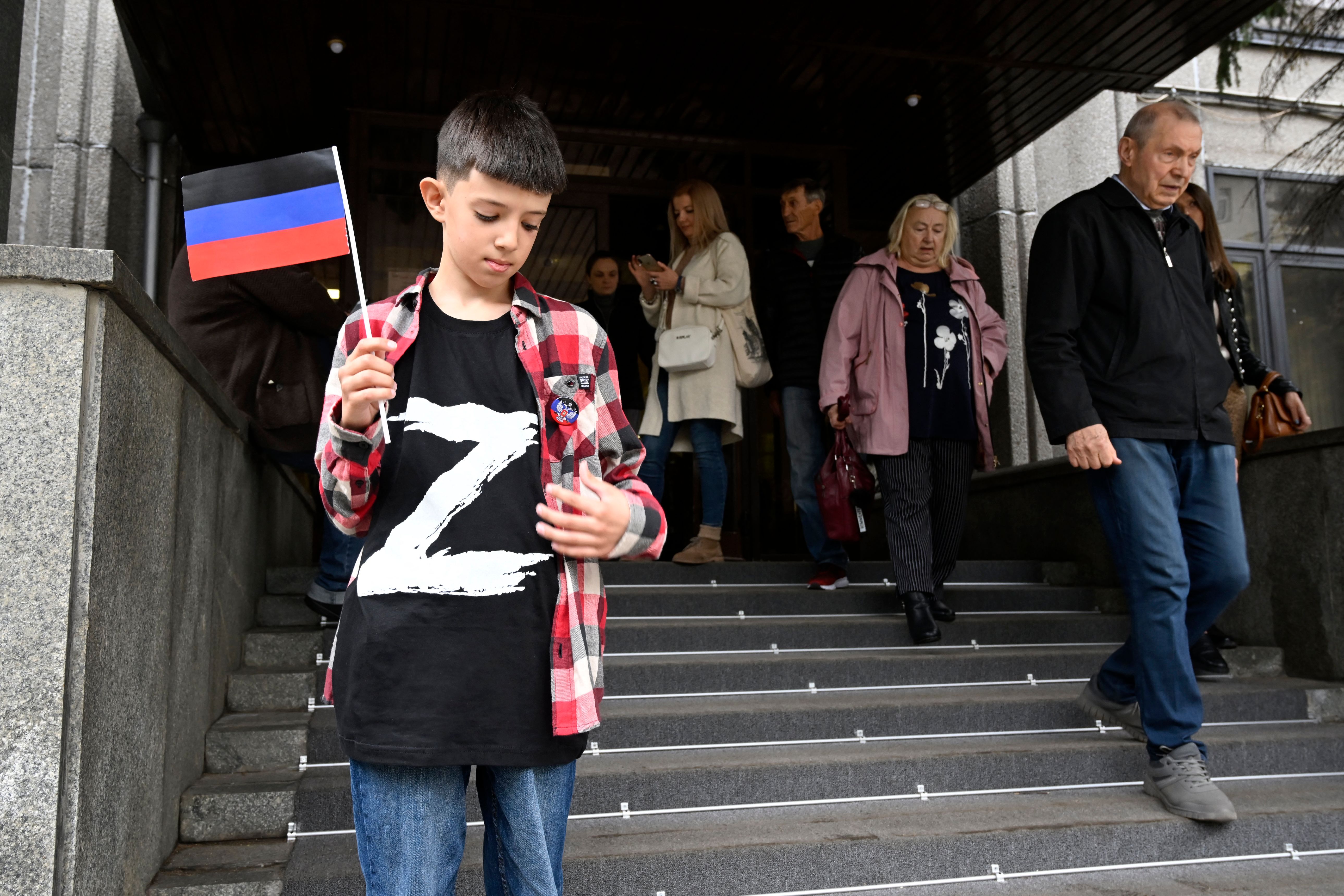 A boy wearing a T-shirt with the letter "Z," the tactical insignia of Russian troops in Ukraine, and holding a flag of the self-proclaimed Donetsk People's Republic, the eastern Ukrainian breakaway region, stands at the entrance to the embassy in Moscow