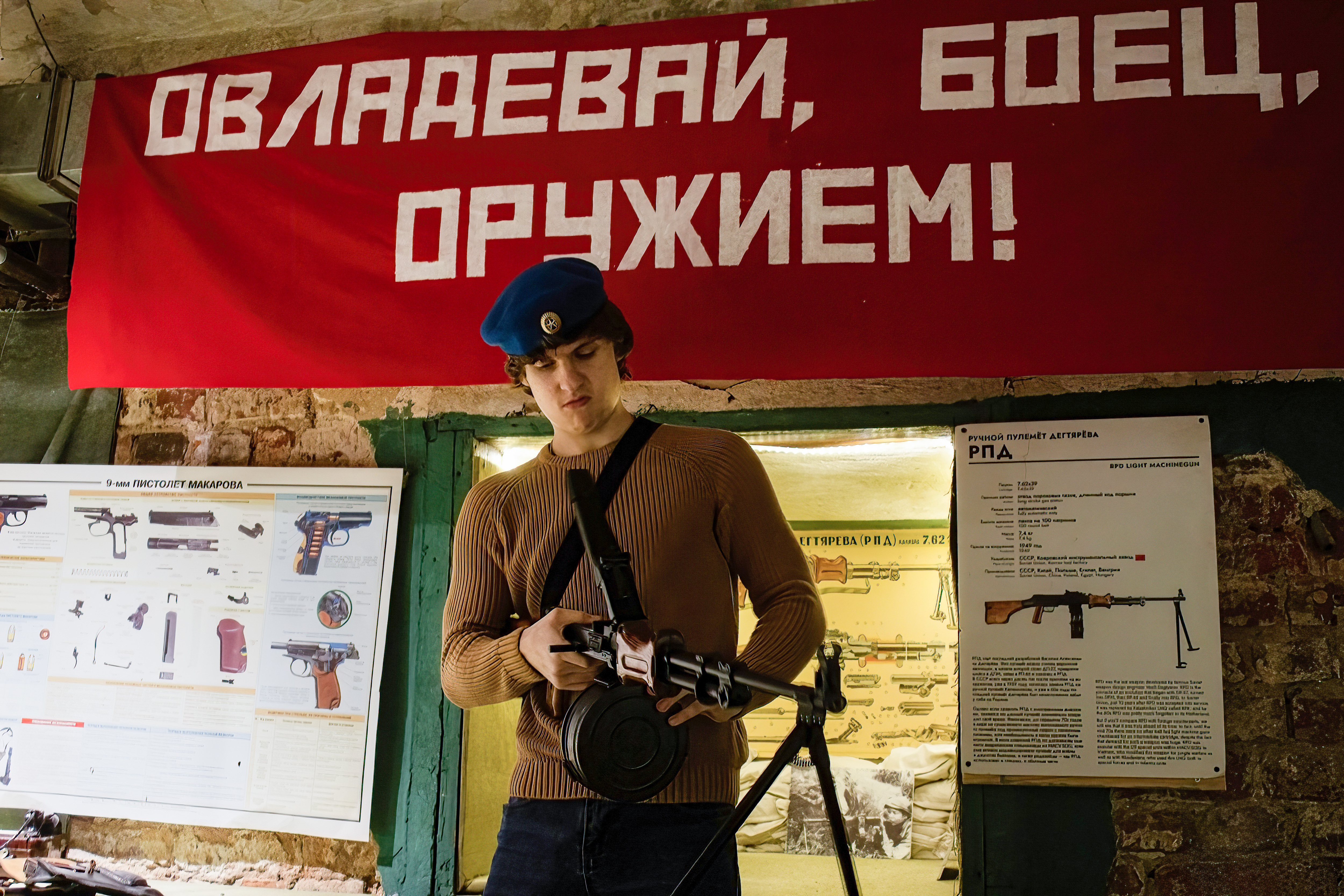 A teenager examines a machine gun, developed in the Soviet Union, at the Guns Dungeon interactive museum in Moscow in 2023. Behind him is a sign with Cyrilllic lettering and museum displays showing different weapons.