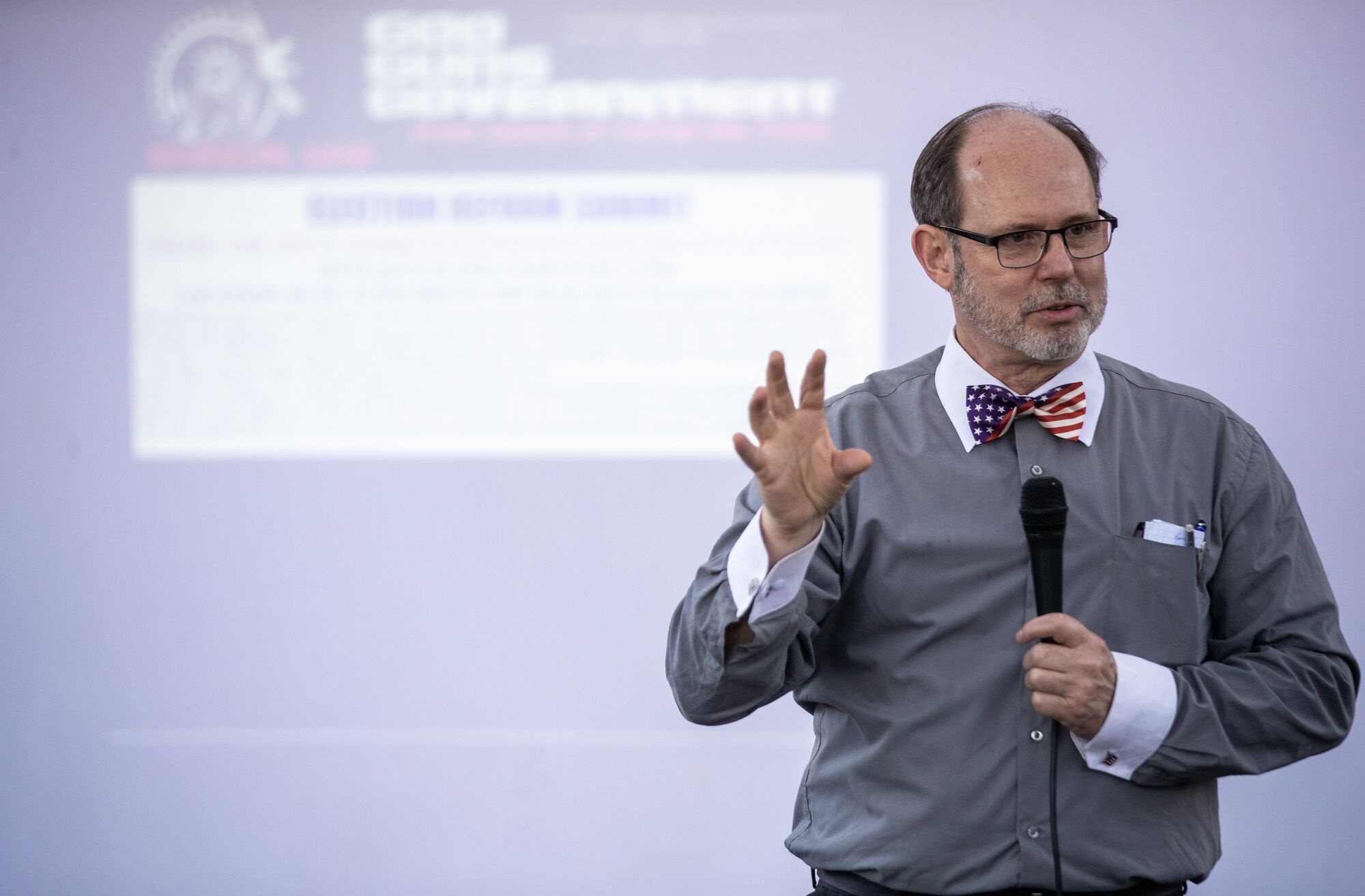 A man speaks into a microphone in front of a screen 