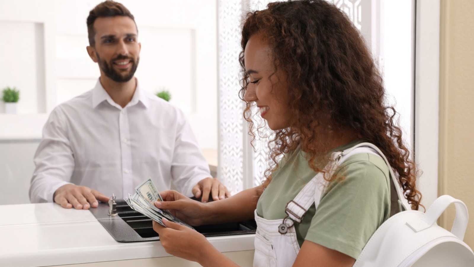 African American woman with money at cash department window in bank. Currency exchange