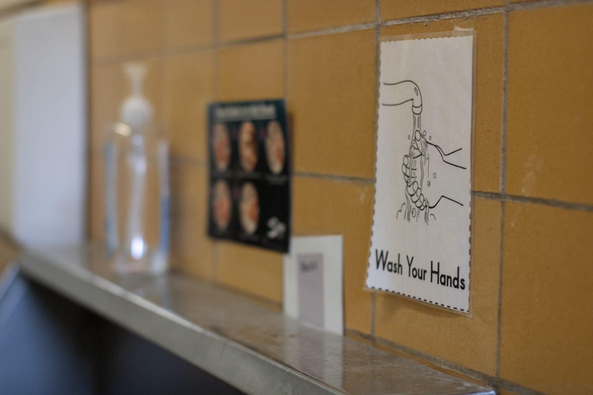 A laminated printout taped to the tiled wall above a sink states 