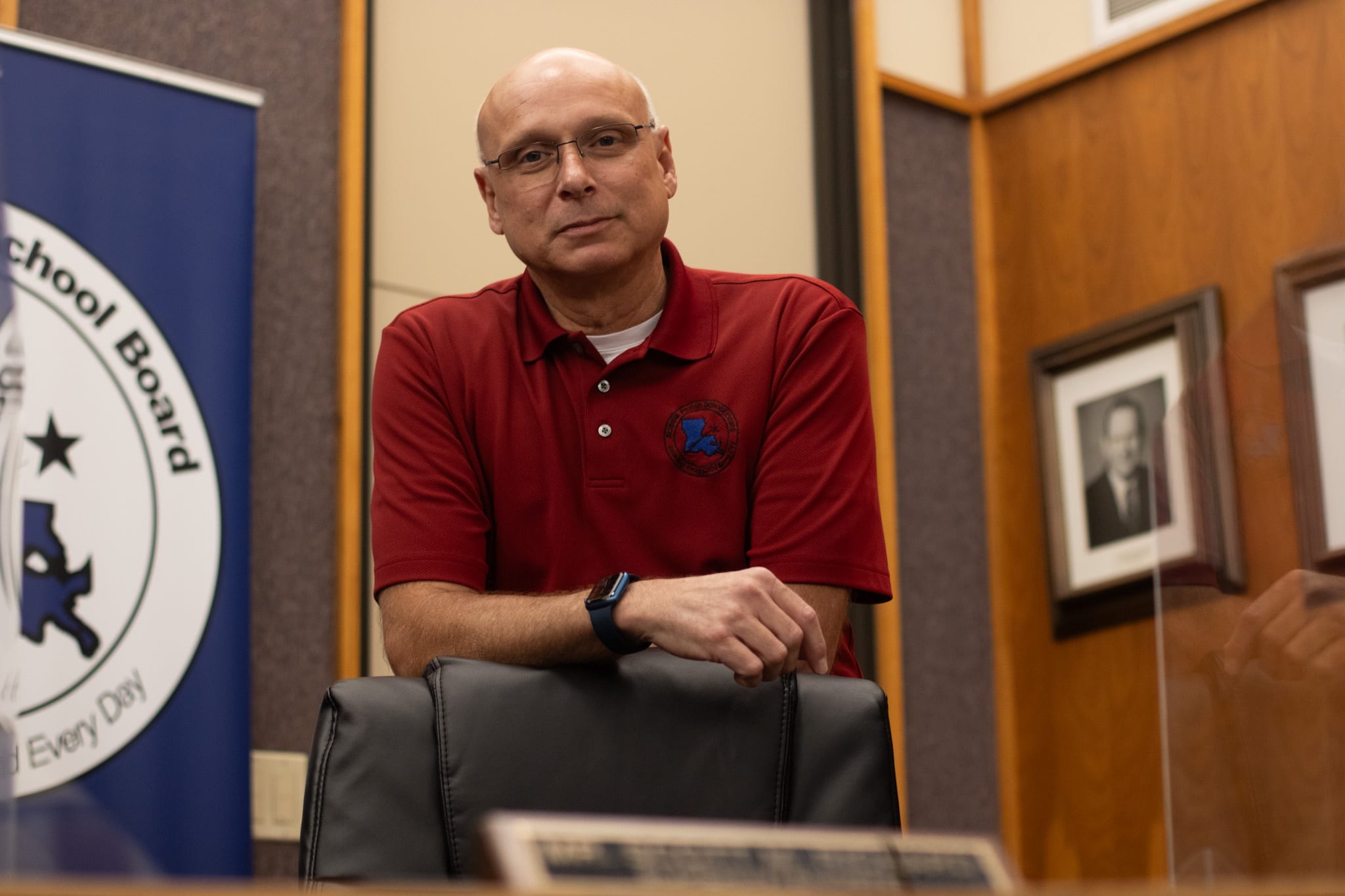 A man in a red polo shirt leans on an office chair.