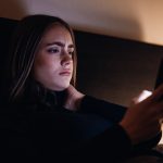 Bad news young woman reading messages on mobile phone lying in bed at night