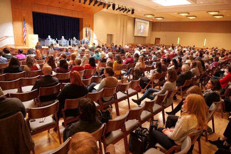 Audience in a crowded hall watch several people on a stage