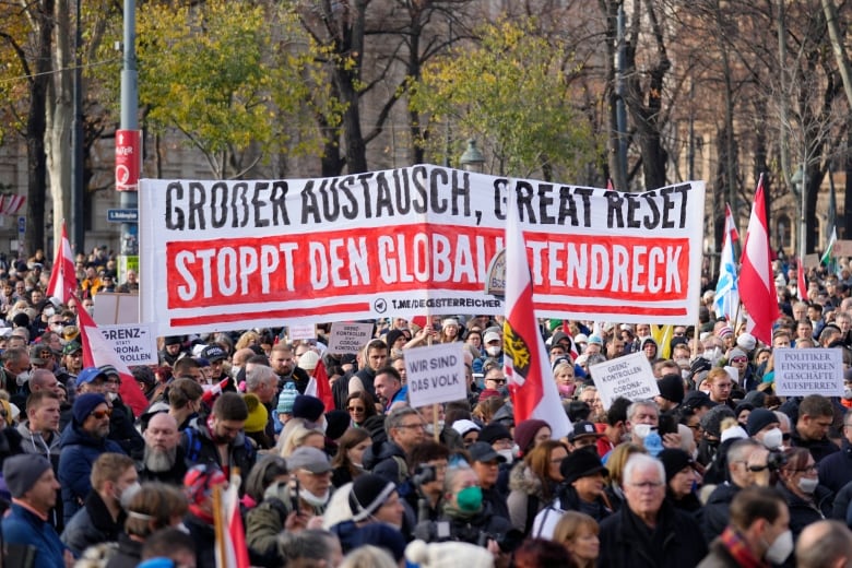 A large crowd of protestors gathered together, in the middle of the group there's a banner reading 'Great exchange, Great Reset, Stop the globalist filth'.