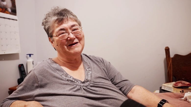 A woman in a grey top sits at a small dining room table. 