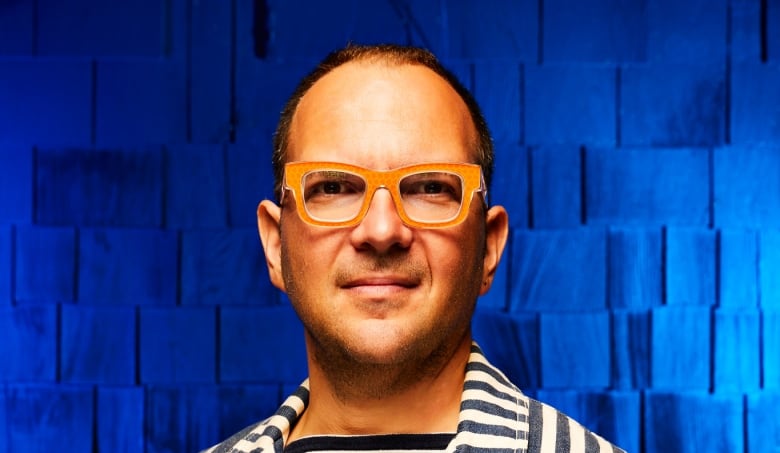 Cory Doctorow wearing a stripped suit with a blue background.