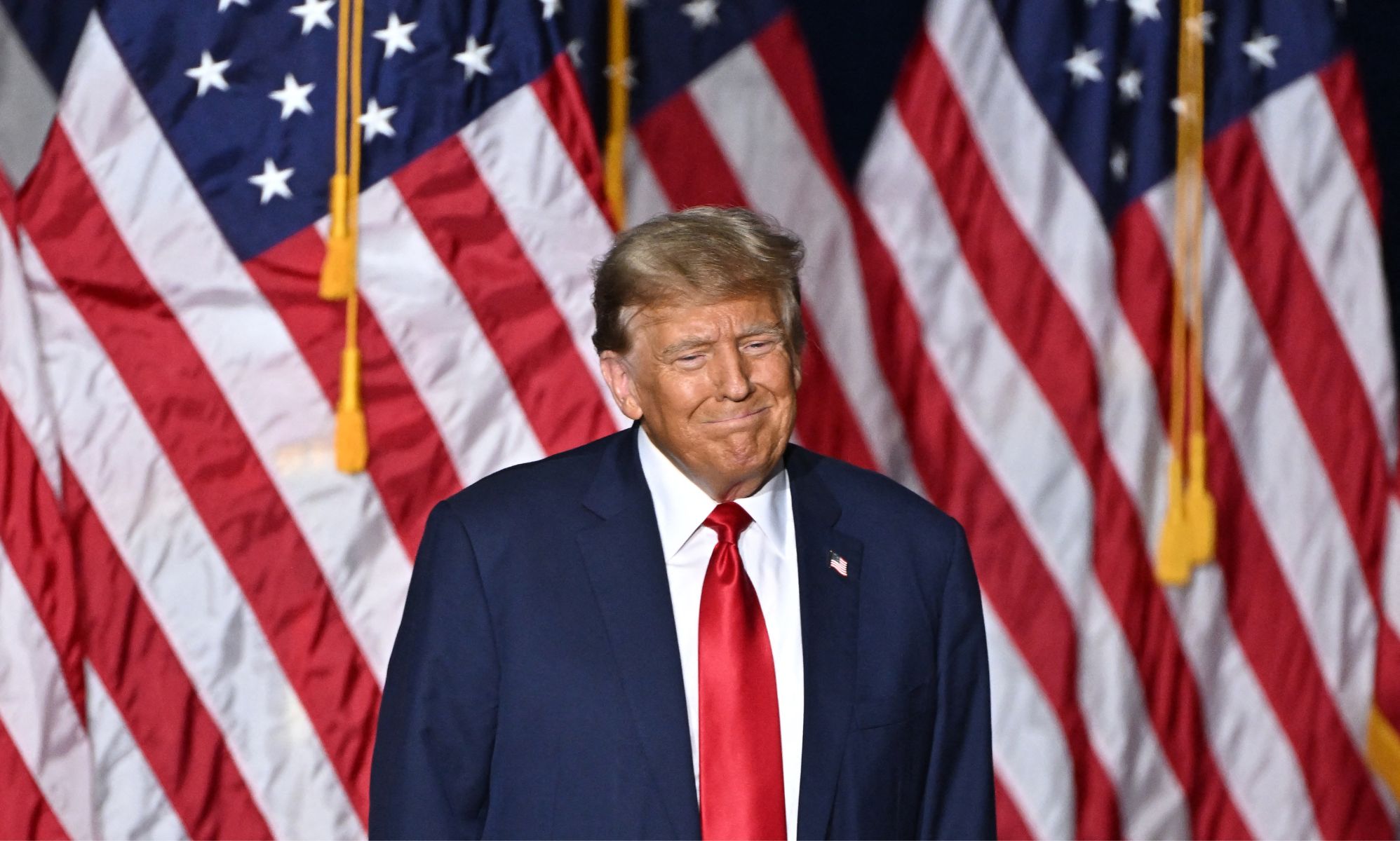 Donald Trump wears a suit and tie as he stands in front of red, white and blue American flags at the Iowa caucus