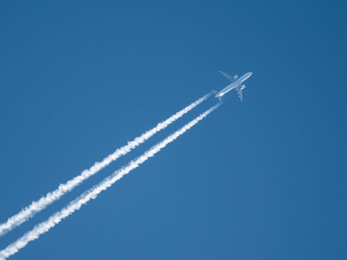 An airplane trails contrails in the blue sky.
