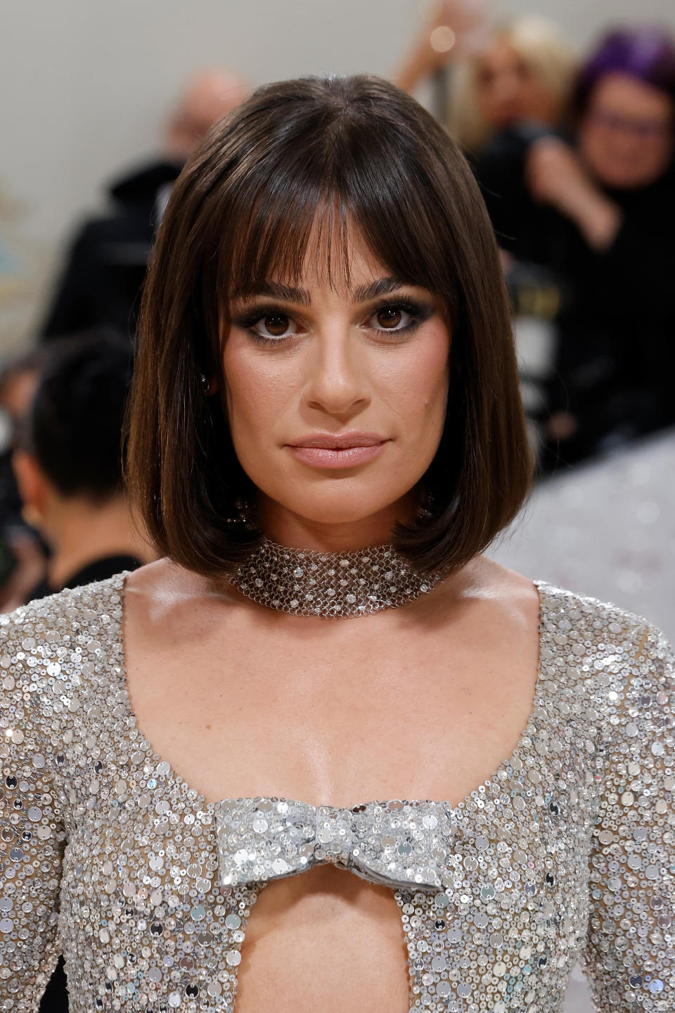 Lea Michele wearing a sparkling silver gown with sequins and a small silver bow at the neckline, attending an event