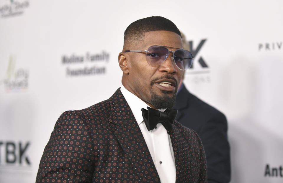 Jamie Foxx in a patterned suit with a black bow tie and sunglasses posing at a formal event