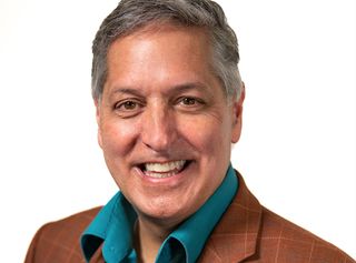 a smiling middle-aged man in a green shirt and brown sports coat