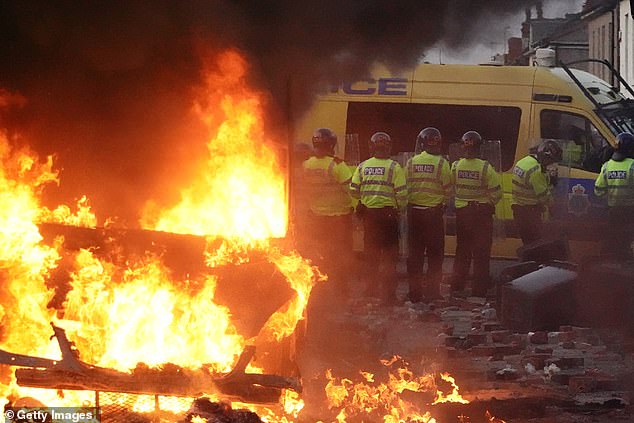 Riot police hold back protesters near a burning police vehicle after disorder broke out on Tuesday night in Southport