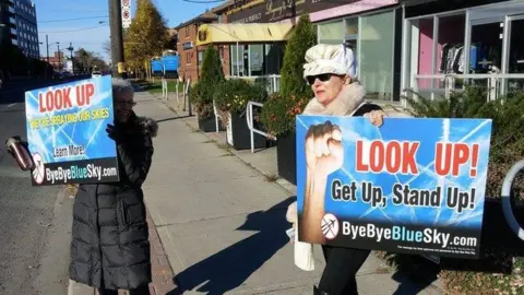 Suzanne Maher Suzanne Maher with Bye Bye Blue Sky anti-chemtrails placard