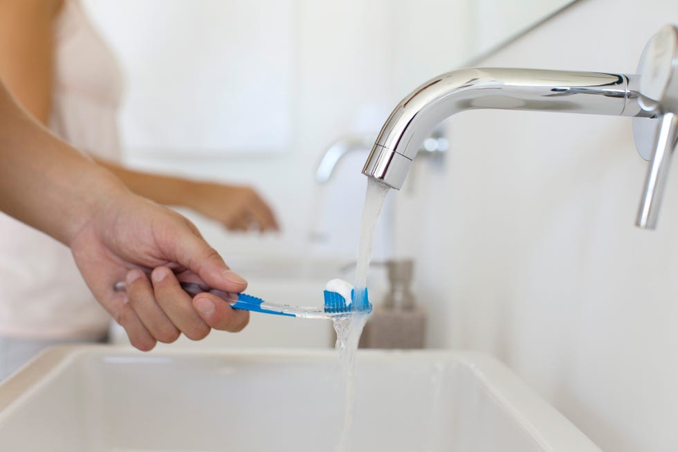 man holding toothbrush under faucet, cropped