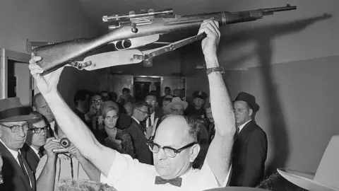 Getty Images A Dallas policeman holds up the rifle used to kill President John F Kennedy on November 22, 1963. Lee Harvey Oswald has been charged with the murder.