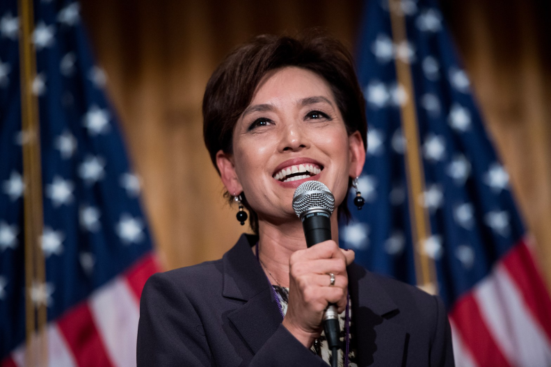 a woman smiles holding a microphone in front of American flags