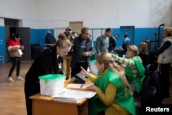 A voter receives her ballot at a polling station during parliamentary elections in the village of Zemo Alvani in the region of Kakheti, Georgia, Oct. 26, 2024.