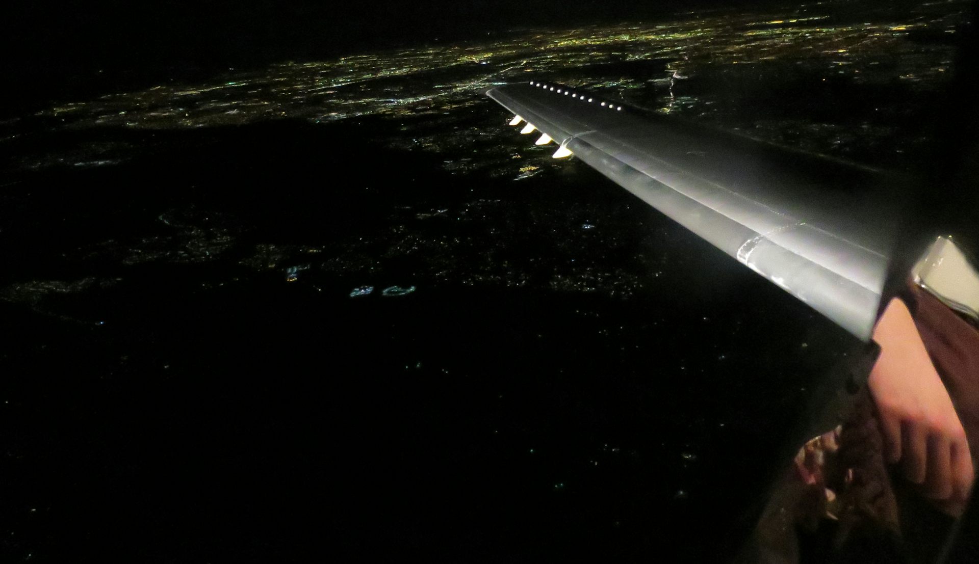 Image taken from a passenger jet of a dark Earth with city lights and a faintly curved horizon