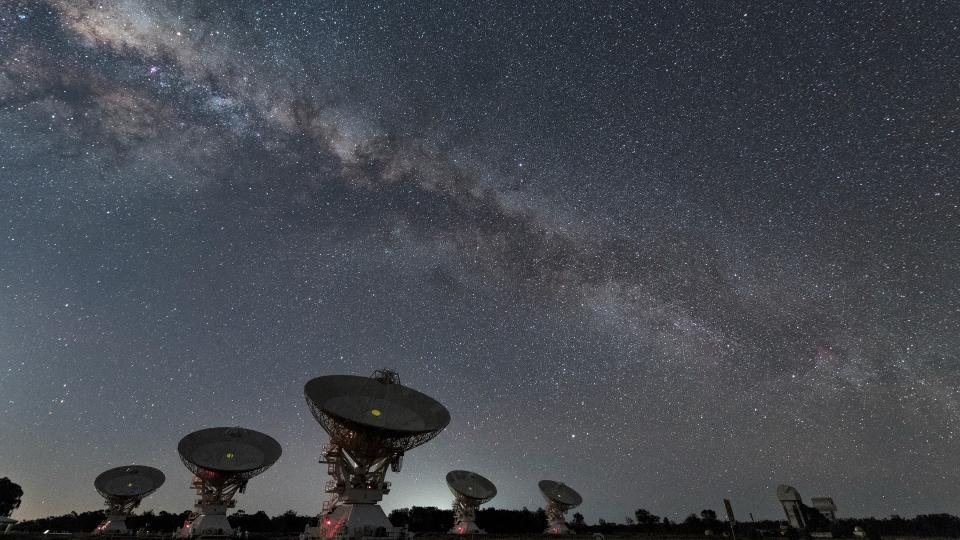  Several large antenna dishes point upward under a starry sky. 