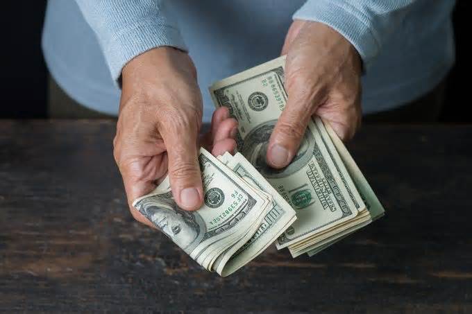 Man holding stack of banknote in both hands doing a payment at old wooden table,high angle view.US banknote.