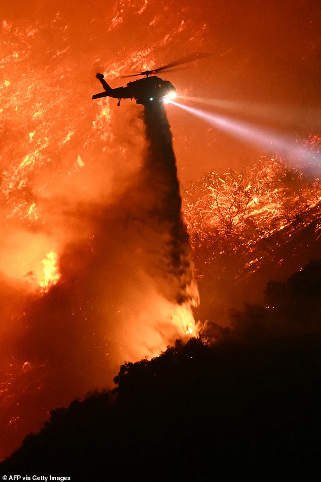 A fire fighting helicopter drops water as the Palisades fire grows near the Mandeville Canyon neighborhood and Encino, California, on January 11, 2025